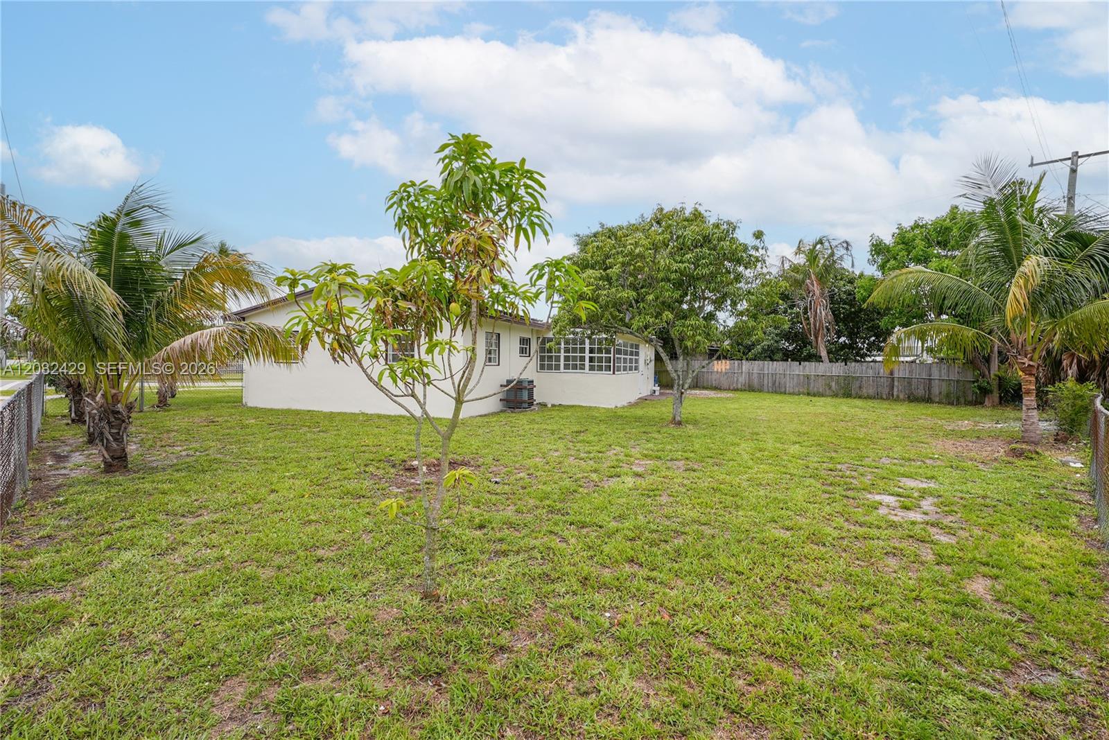 A backyard with a lawn, several trees, and the exterior of a white house — 701 NW 176th Ter, Miami Gardens FL 33169, MIAMI GARDENS, FL