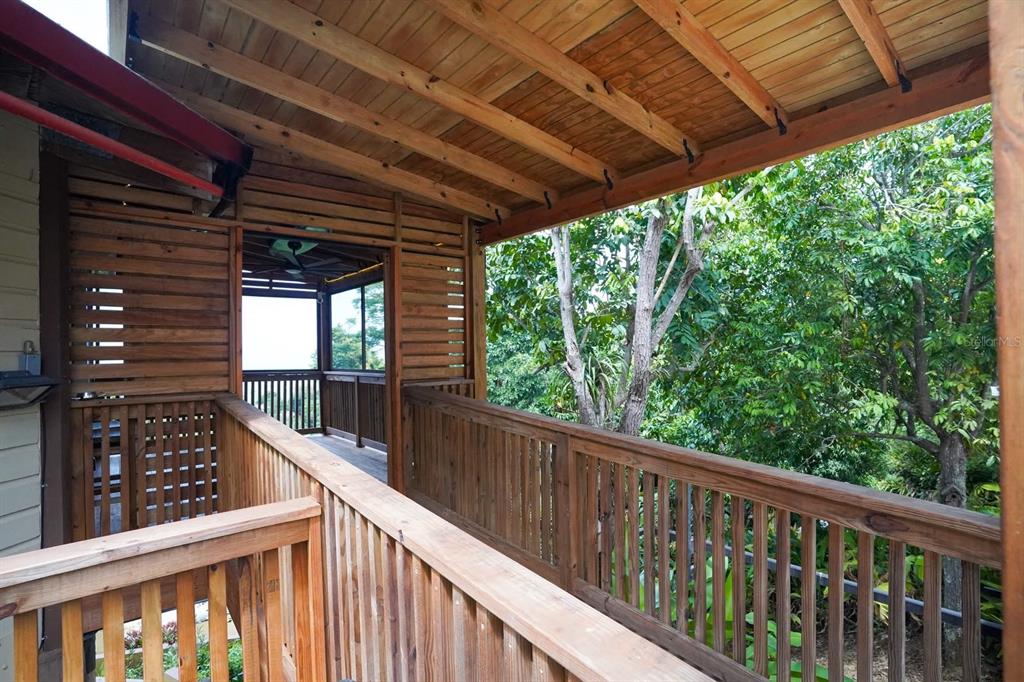 A wooden balcony with a slatted privacy wall overlooks lush green trees — LOT 2 B URB VILLAS DE MONTE VERDE, PONCE, PR