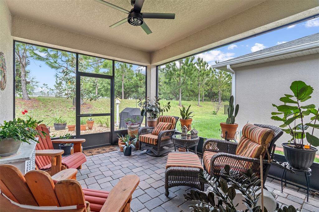 A screened-in patio with wicker furniture, potted plants, and a ceiling fan overlooking a yard — 3113 SONGBIRD CIR, ST CLOUD, FL