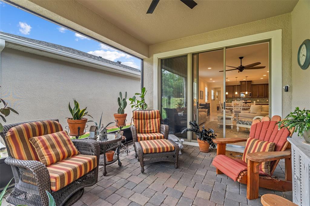 A covered patio features paver flooring, wicker furniture with striped cushions, and potted plants — 3113 SONGBIRD CIR, ST CLOUD, FL