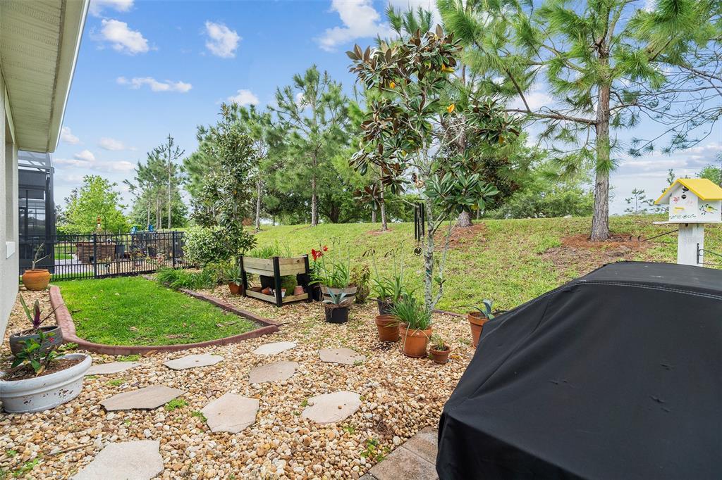 A backyard patio features a gravel ground, potted plants, a raised garden bed, and trees — 3113 SONGBIRD CIR, ST CLOUD, FL