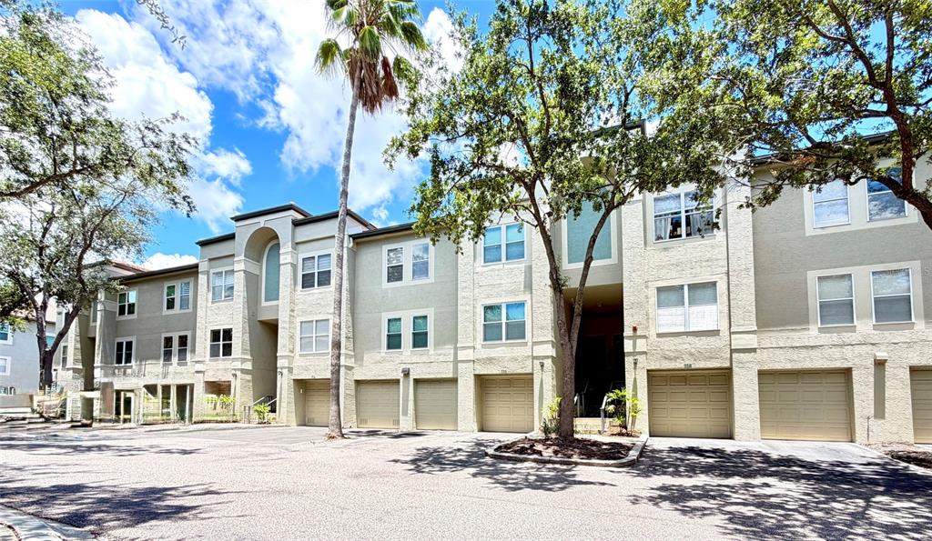 A multi-story apartment building with beige stucco siding, multiple garage doors, and surrounding trees — 724 CORAL REEF DRIVE, TAMPA, FL
