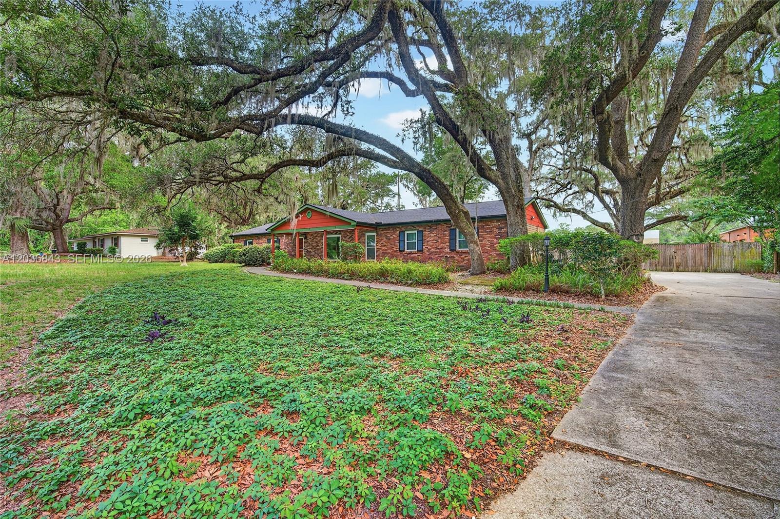 A brick ranch-style house sits behind a large lawn shaded by mature oak trees — 1944 SW 48th Avenue, Gainesville FL 32608, GAINESVILLE, FL