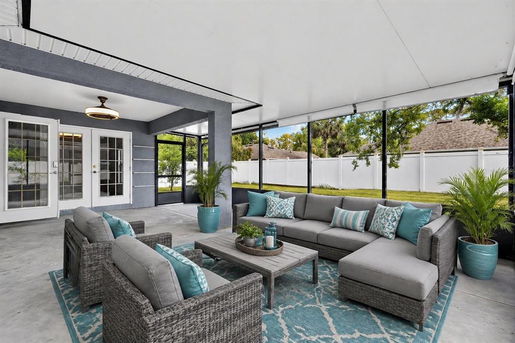 A screened-in patio features gray wicker furniture, a blue patterned rug, and a concrete floor — 23 ESSINGTON LANE, PALM COAST, FL