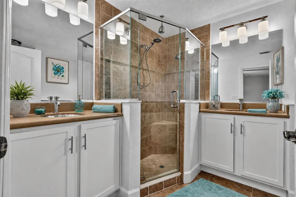 A bathroom features white cabinets, dual sinks, and a central glass-enclosed shower with brown tiles — 23 ESSINGTON LANE, PALM COAST, FL