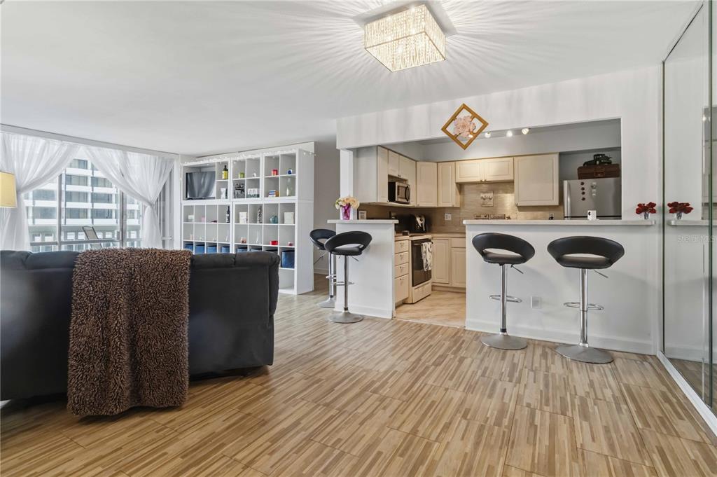 A living room with wood-look tile floors, a kitchen breakfast bar, and white shelving units — 2800 N ATLANTIC AVENUE UNIT 1105, DAYTONA BEACH, FL