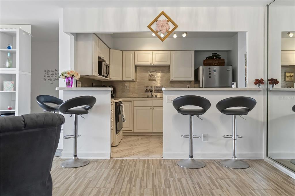 A kitchen with white cabinets and stainless steel appliances features a breakfast bar with stools — 2800 N ATLANTIC AVENUE UNIT 1105, DAYTONA BEACH, FL