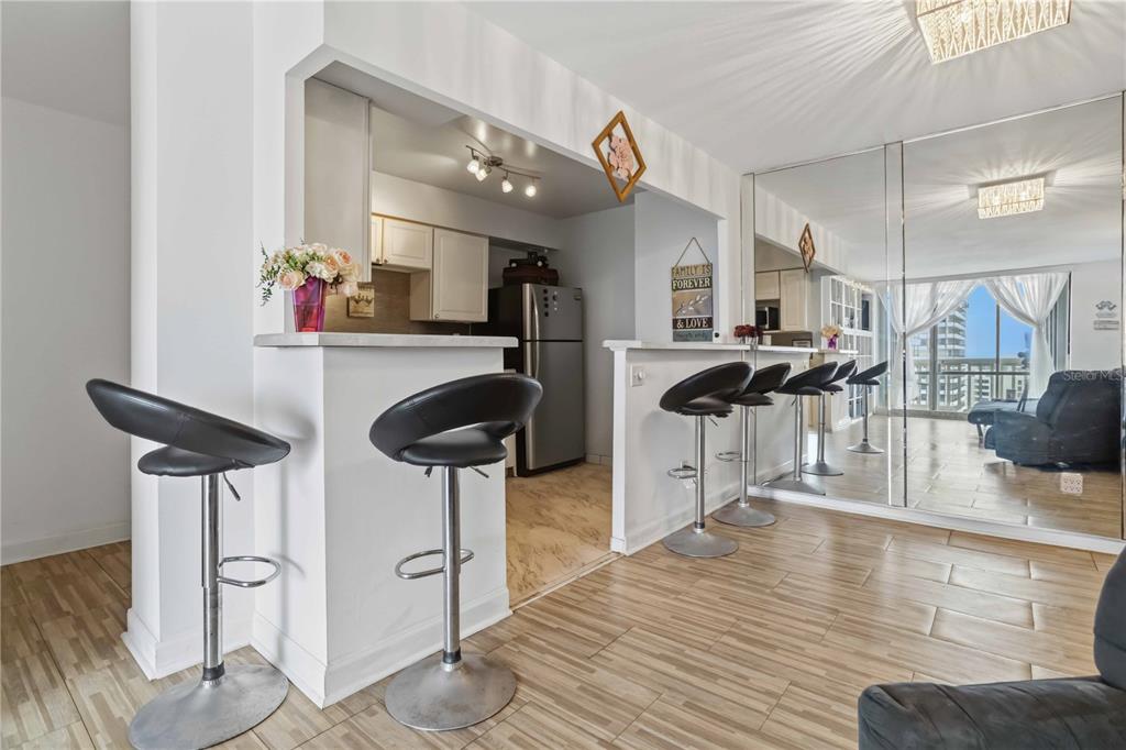 A kitchen with a breakfast bar and stools opens into a living area with mirrored walls — 2800 N ATLANTIC AVENUE UNIT 1105, DAYTONA BEACH, FL