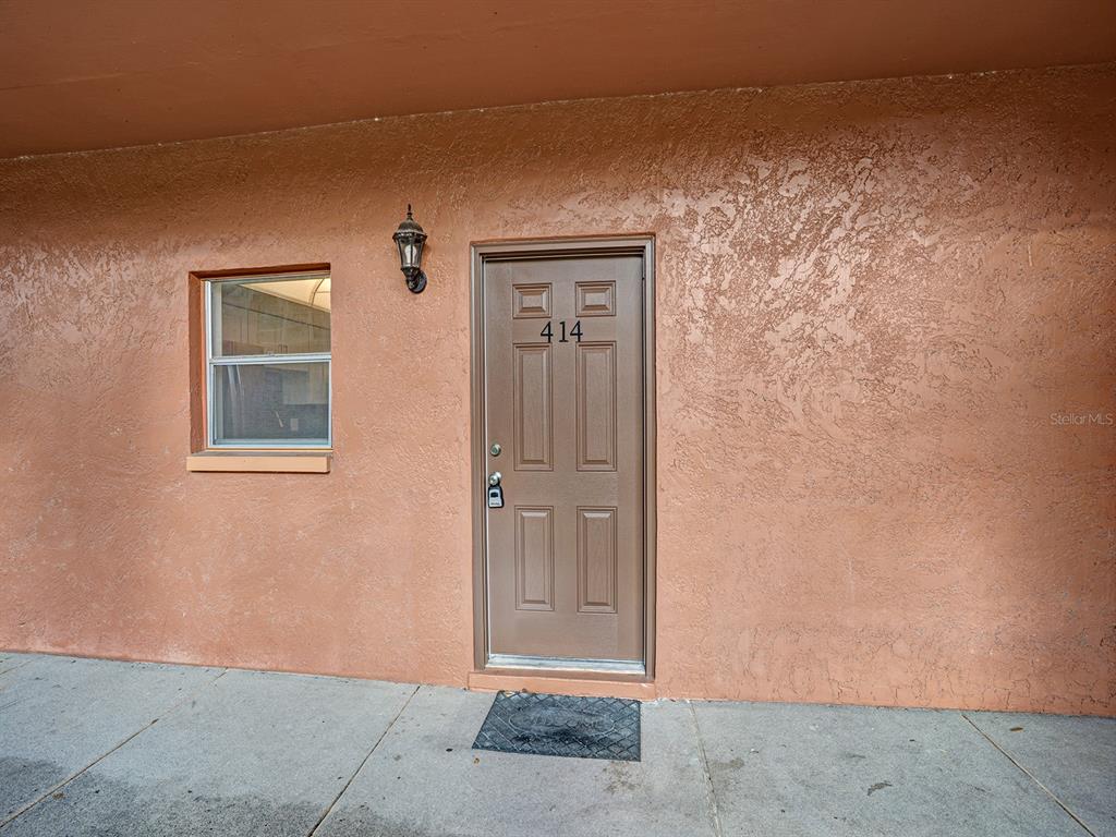 A brown front door with the number 414 is set into a textured peach-colored exterior wall — 4805 ALT 19 UNIT 414, PALM HARBOR, FL
