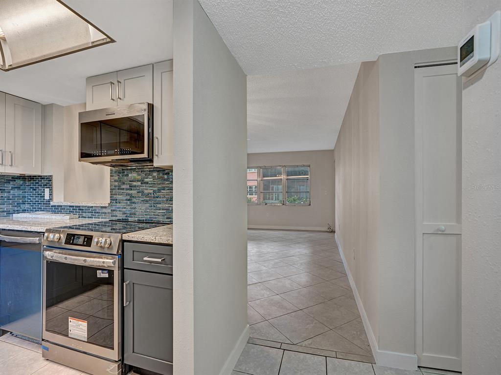 A kitchen with gray cabinets and a blue tile backsplash opens into a tiled living area — 4805 ALT 19 UNIT 414, PALM HARBOR, FL