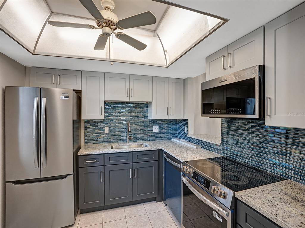 A kitchen features gray cabinets, stainless steel appliances, granite countertops, and a blue glass backsplash — 4805 ALT 19 UNIT 414, PALM HARBOR, FL