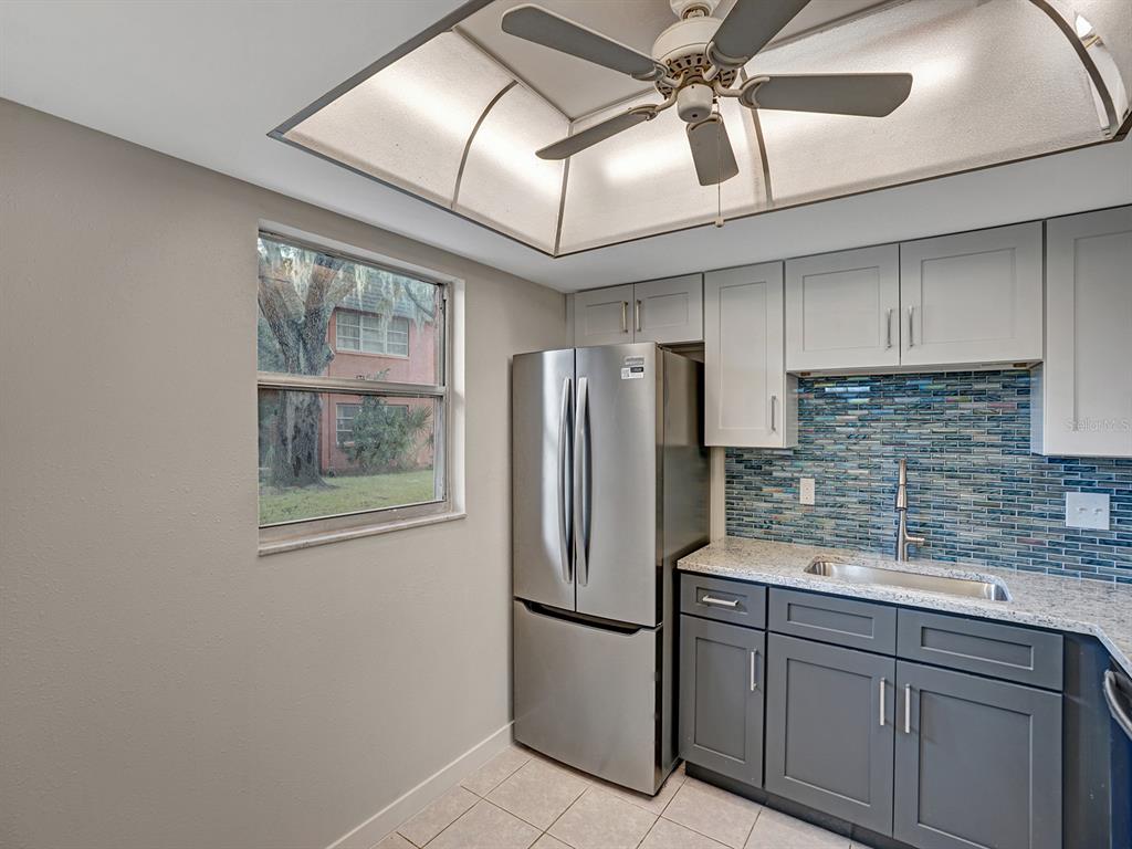 A kitchen features gray lower cabinets, white upper cabinets, a stainless refrigerator, and blue backsplash tile — 4805 ALT 19 UNIT 414, PALM HARBOR, FL