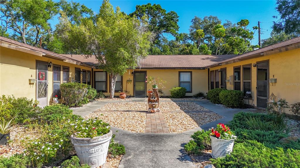 A U-shaped apartment complex features a central courtyard with gravel, landscaping, and a fountain — 2006 7TH AVENUE W UNIT B, BRADENTON, FL