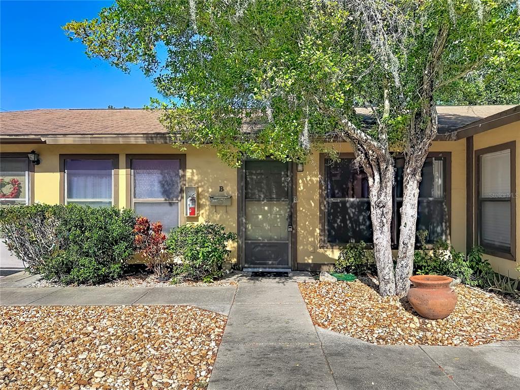 A yellow exterior wall features a front door, windows, and a tree in the yard — 2006 7TH AVENUE W UNIT B, BRADENTON, FL