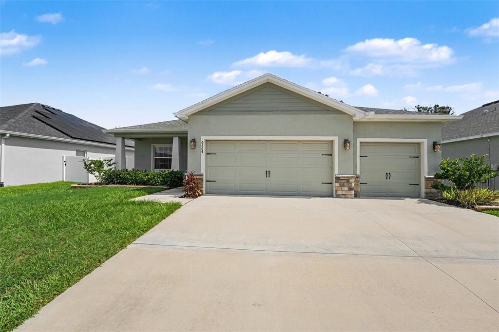 A single-story house with a three-car garage and a concrete driveway under a blue sky — 6864 MOSSY OAK LANE, LAKELAND, FL