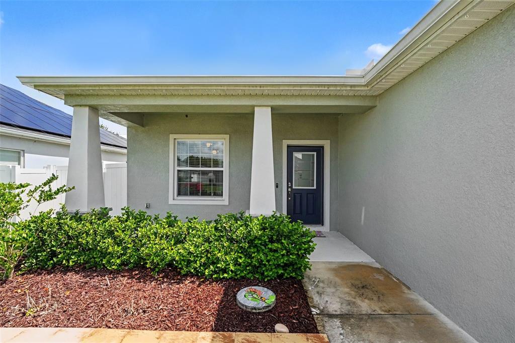 A covered front porch features a dark blue door, a window, and a green hedge — 6864 MOSSY OAK LANE, LAKELAND, FL