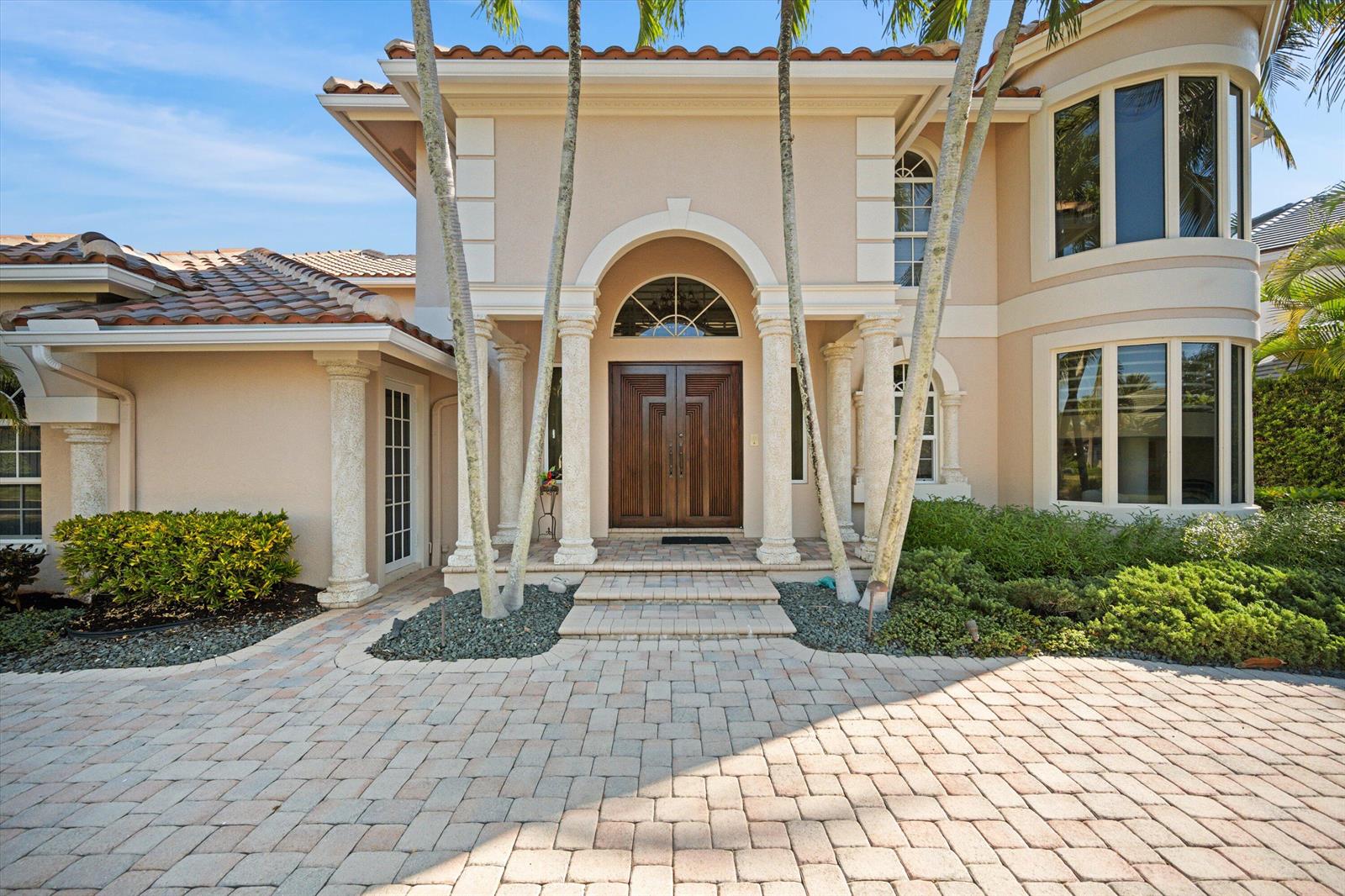 A beige two-story house features a paved driveway, arched entryway, and double wooden front doors — 3164 Casseekey Island Road, Jupiter FL 33477, JUPITER, FL