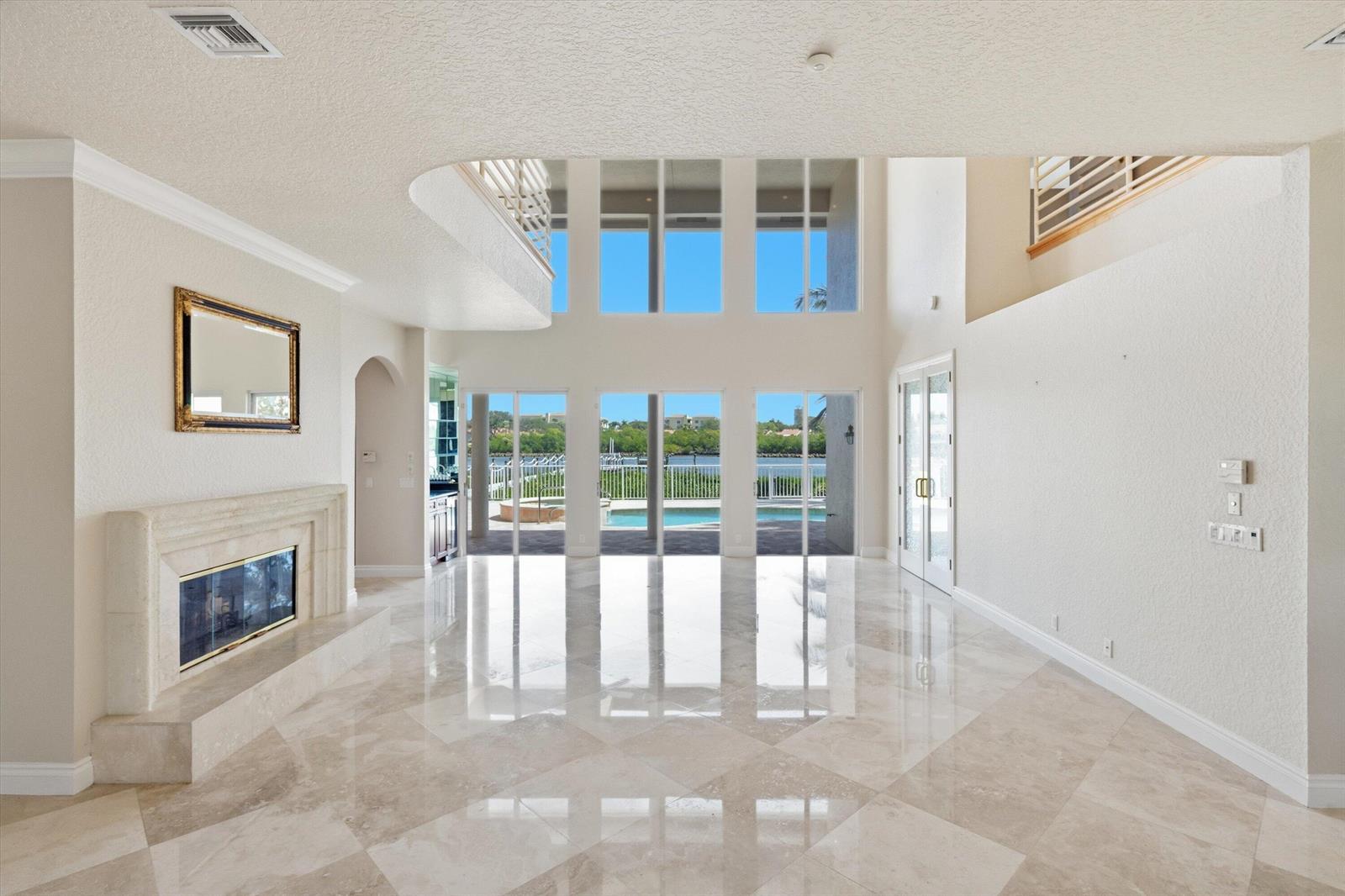 A spacious living room features high ceilings, marble floors, a fireplace, and floor-to-ceiling windows — 3164 Casseekey Island Road, Jupiter FL 33477, JUPITER, FL