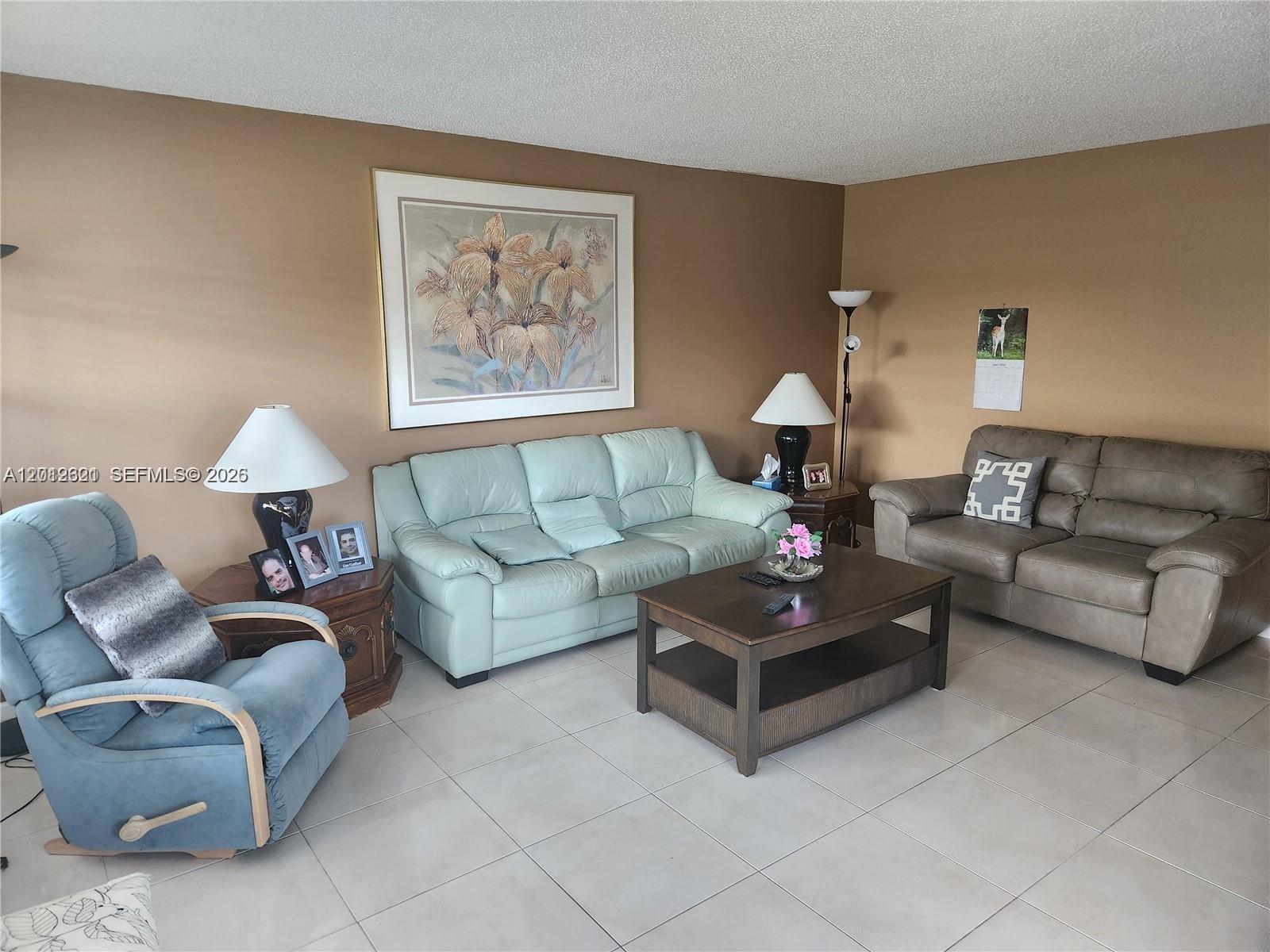 A living room features light-colored tile floors, tan walls, and a mix of seating furniture — DEERFIELD BEACH, FL