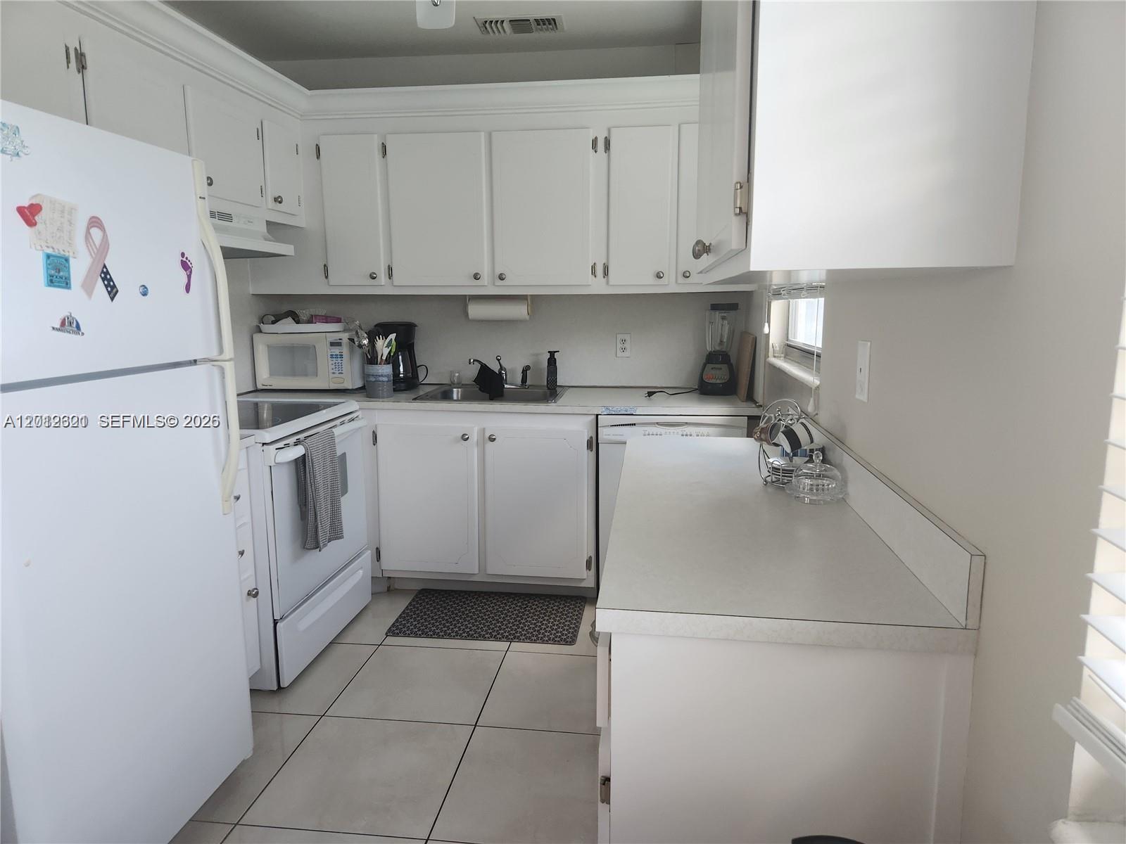 A kitchen features white cabinets, white appliances, light countertops, and tiled flooring — DEERFIELD BEACH, FL