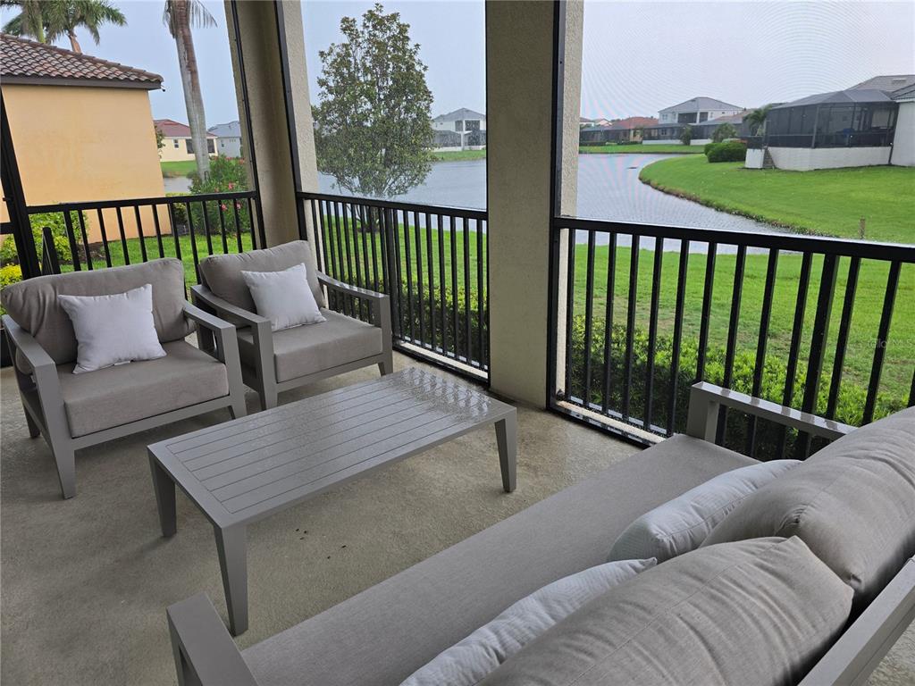 A screened-in patio features outdoor furniture overlooking a pond and neighboring houses — 5815 INSPIRATION TERRACE, BRADENTON, FL