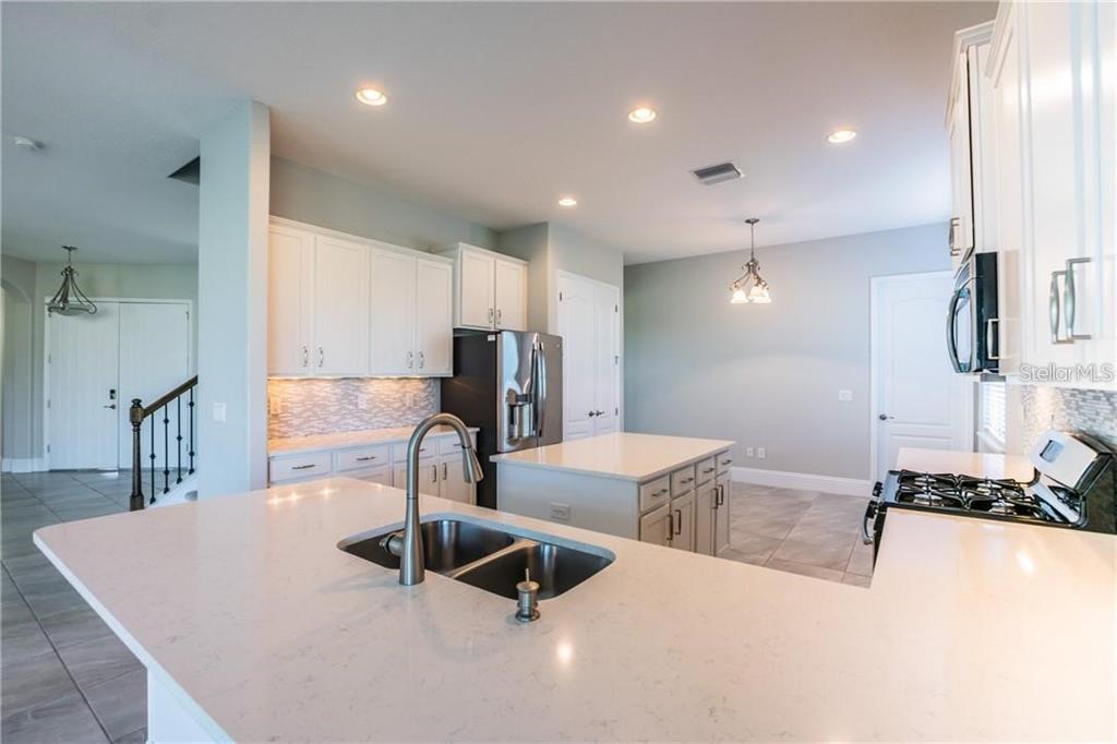 A modern kitchen features white cabinets, quartz countertops, a central island, and stainless steel appliances — 5815 INSPIRATION TERRACE, BRADENTON, FL