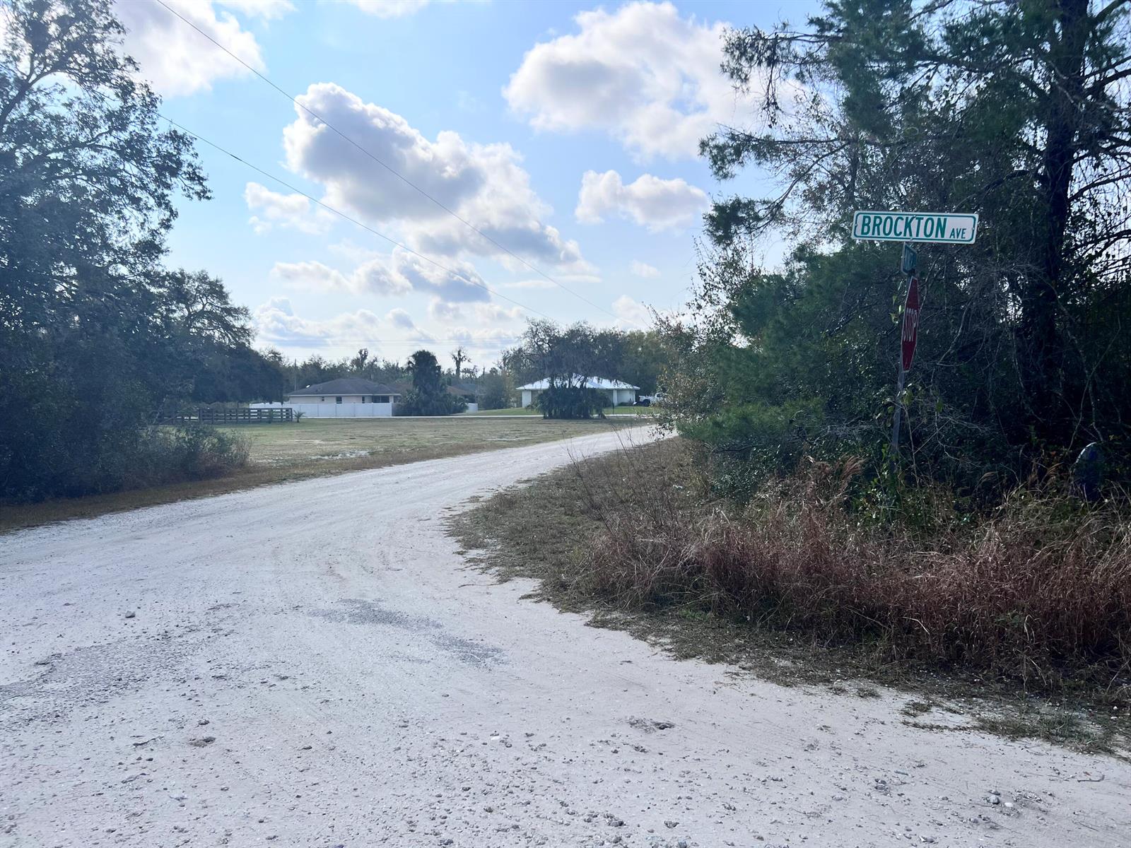 A dirt road leads toward houses under a cloudy sky near a Brockton Ave sign — 4847 Brockton Avenue, FL 33875, FL