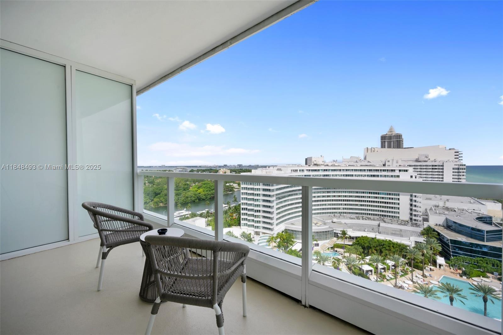 A balcony with two chairs and a small table overlooks a large resort complex — 4391 Collins Ave # 1605, Miami Beach FL 33140, MIAMI BEACH, FL