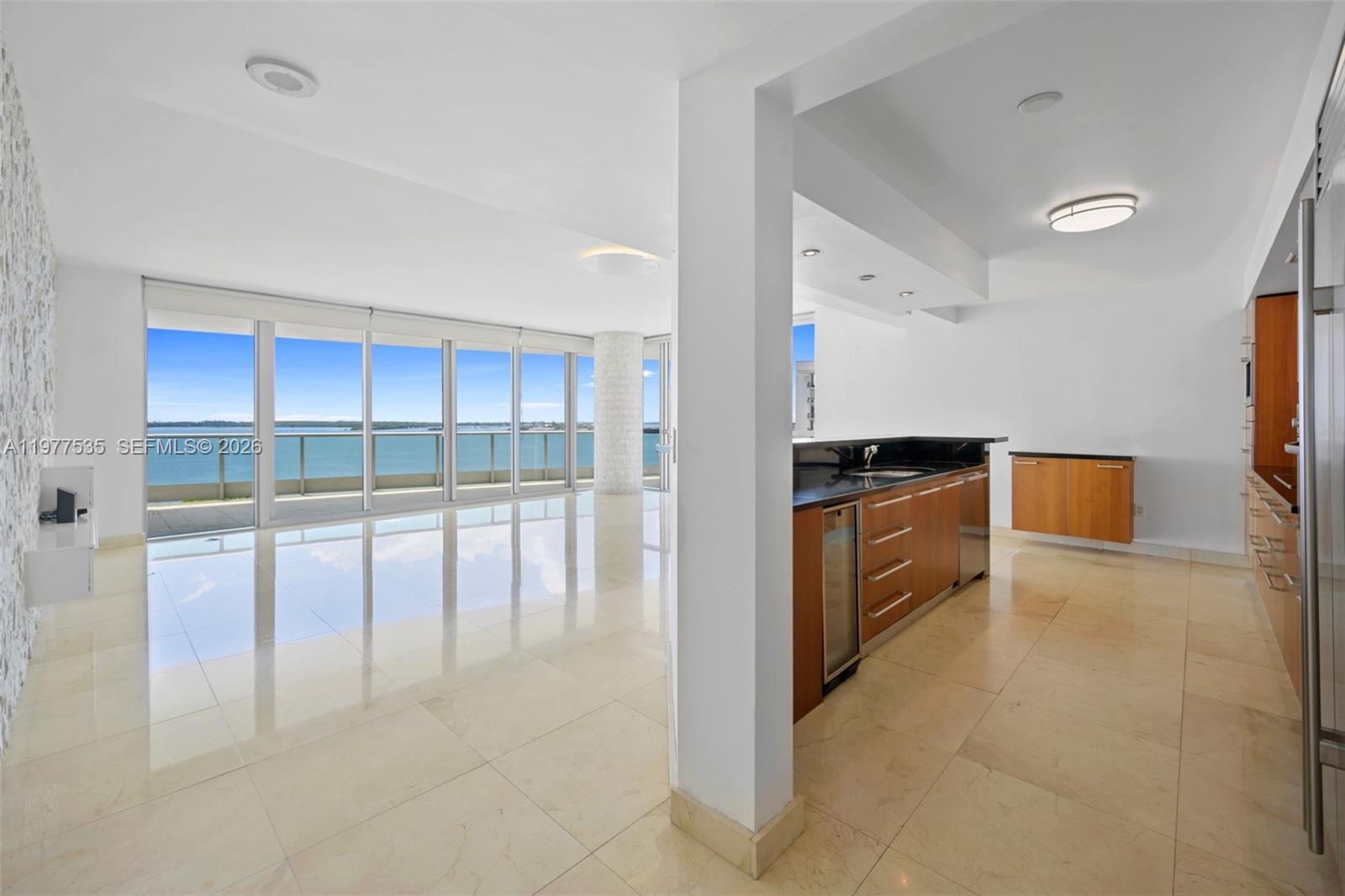 A modern kitchen with wood cabinets and stone floors opens to a bright living area — 1331 Brickell Bay Dr # 911, Miami FL 33131, MIAMI, FL