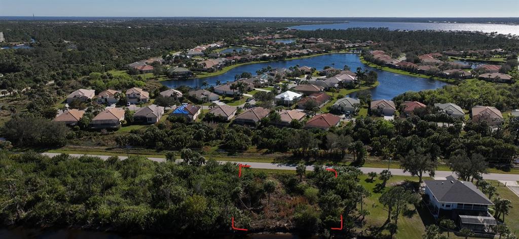 An aerial view shows a vacant, wooded lot outlined in red next to a waterfront neighborhood — 13338 PRENTICE AVENUE, PORT CHARLOTTE, FL