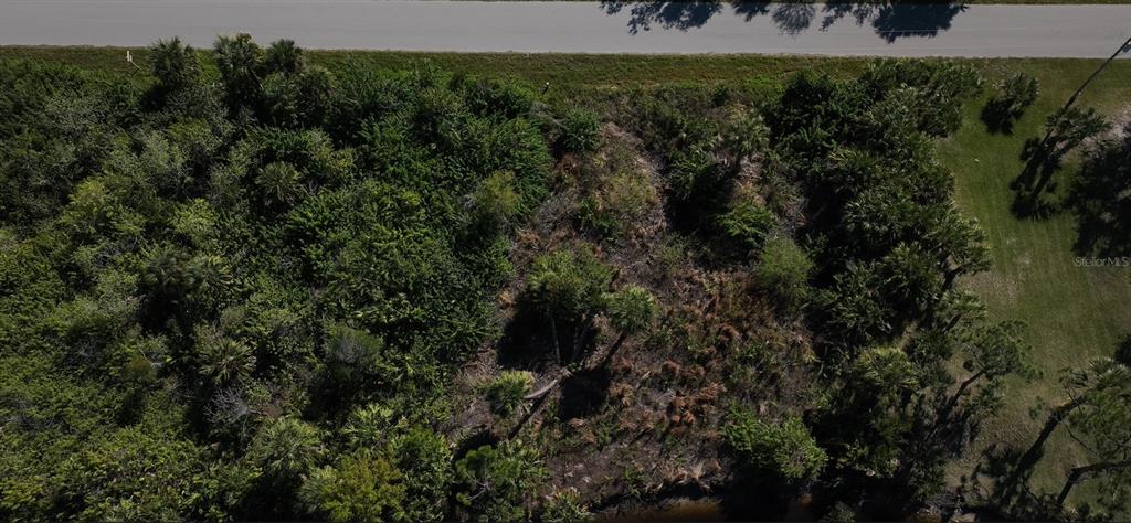 An aerial view shows a vacant, wooded lot bordering a road and a small body of water — 13338 PRENTICE AVENUE, PORT CHARLOTTE, FL