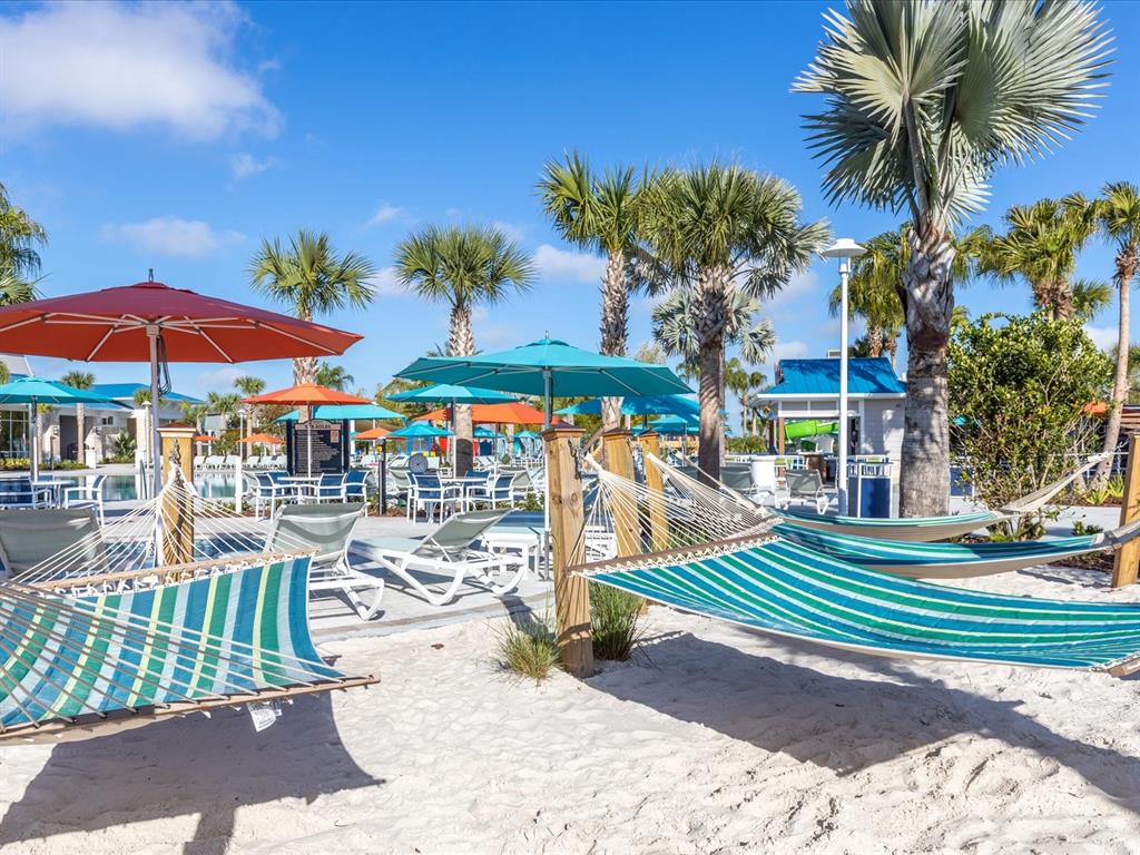 A sandy beach area features several striped hammocks, patio umbrellas, and palm trees — 3044 MAHALO DRIVE, DAVENPORT, FL
