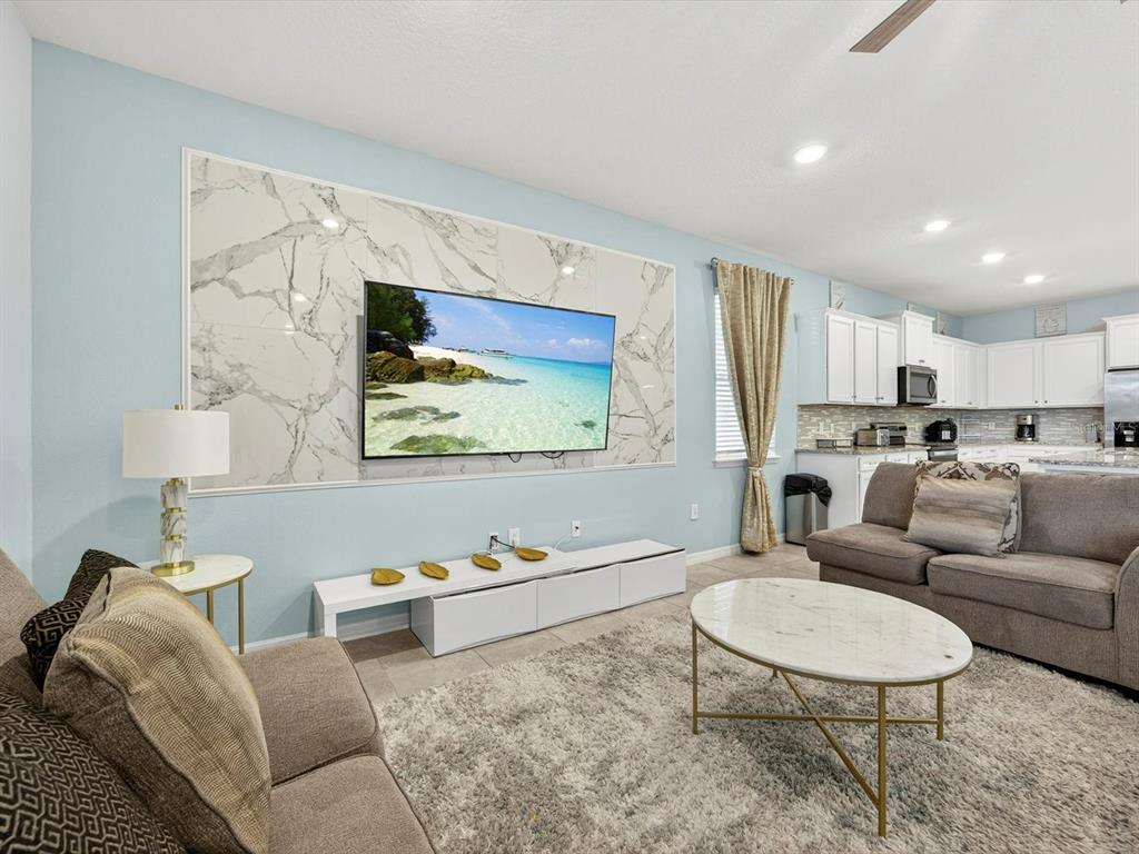A living room features a marble-tiled accent wall with a mounted television and white furniture — 3044 MAHALO DRIVE, DAVENPORT, FL