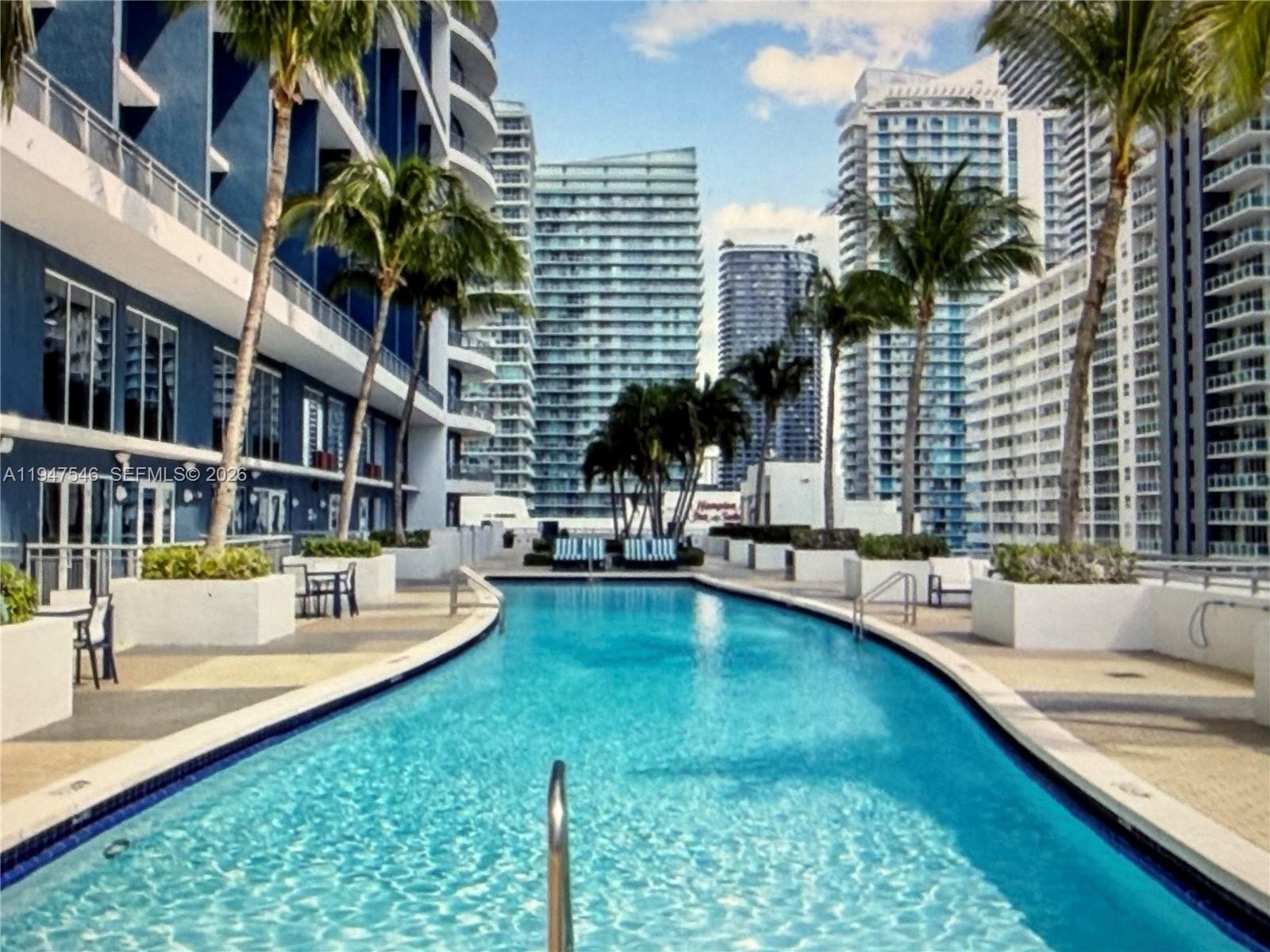 An outdoor swimming pool is surrounded by palm trees and tall modern apartment buildings — 60 SW 13th St # 3214, Miami FL 33130, MIAMI, FL