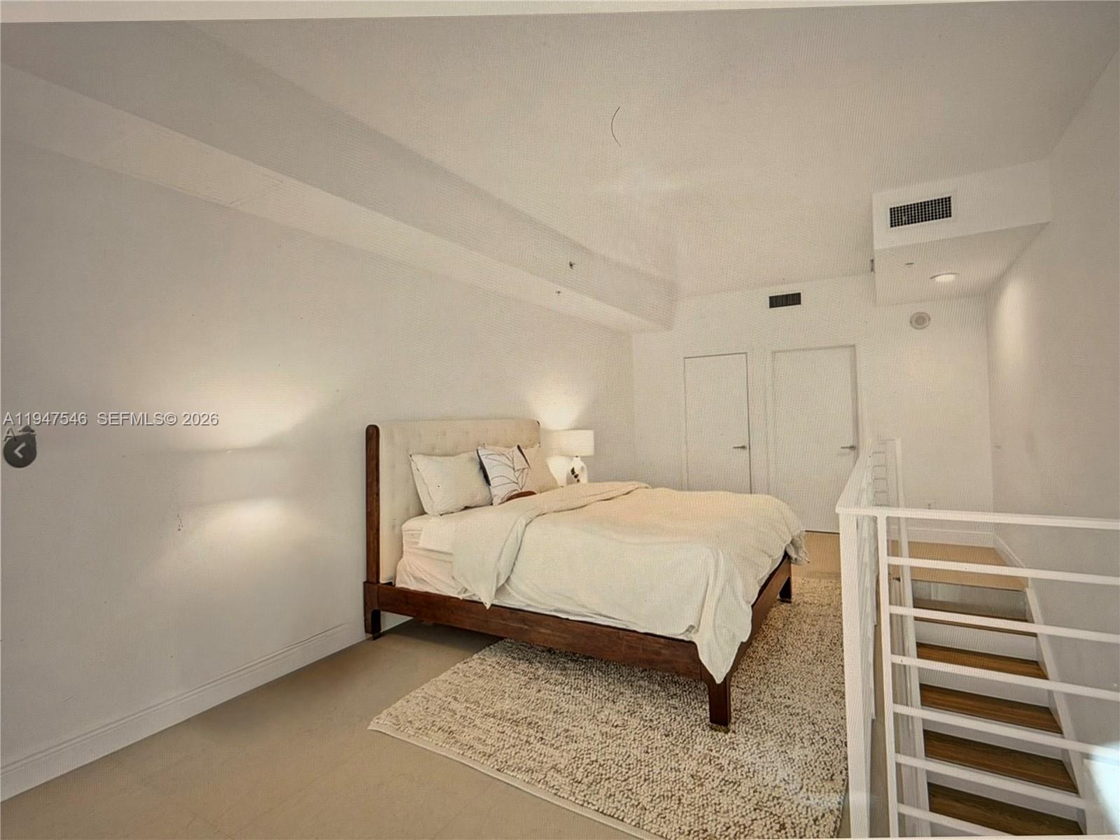 A bedroom features a bed on a rug next to a staircase with white railings — 60 SW 13th St # 3214, Miami FL 33130, MIAMI, FL