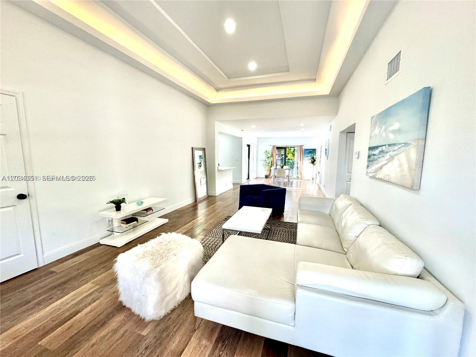 A living room features a white sectional sofa, tray ceiling, and wood-look flooring — EL PORTAL, FL
