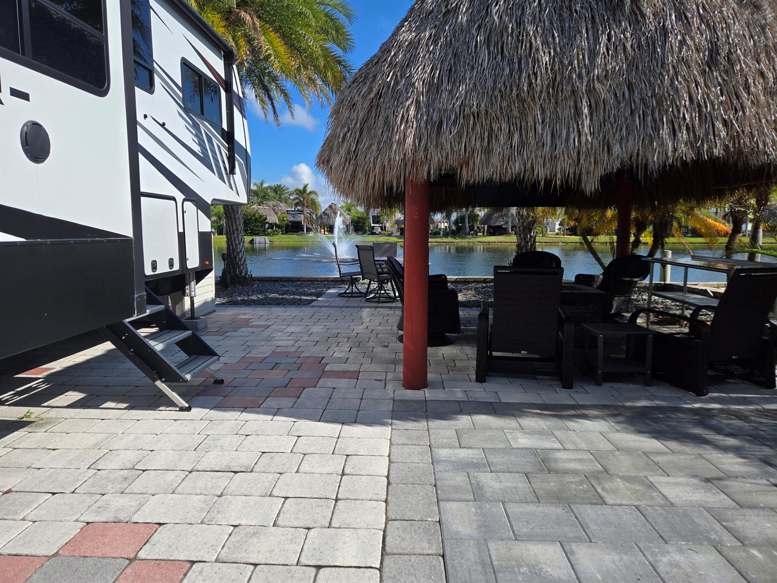 A patio with a tiki hut and outdoor furniture overlooks a pond with a fountain — 609 SW 42nd Cove, Okeechobee FL 34974, OKEECHOBEE, FL
