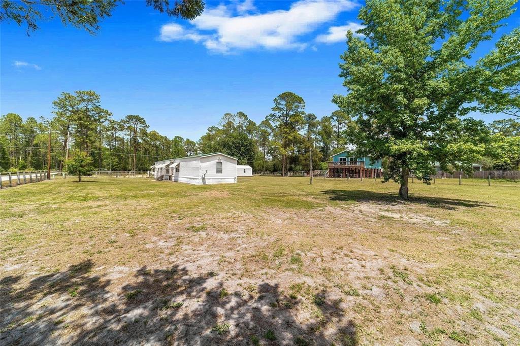 A white mobile home sits on a large, grassy lot with trees in the background — 13261 NE 155TH LANE, FORT MC COY, FL