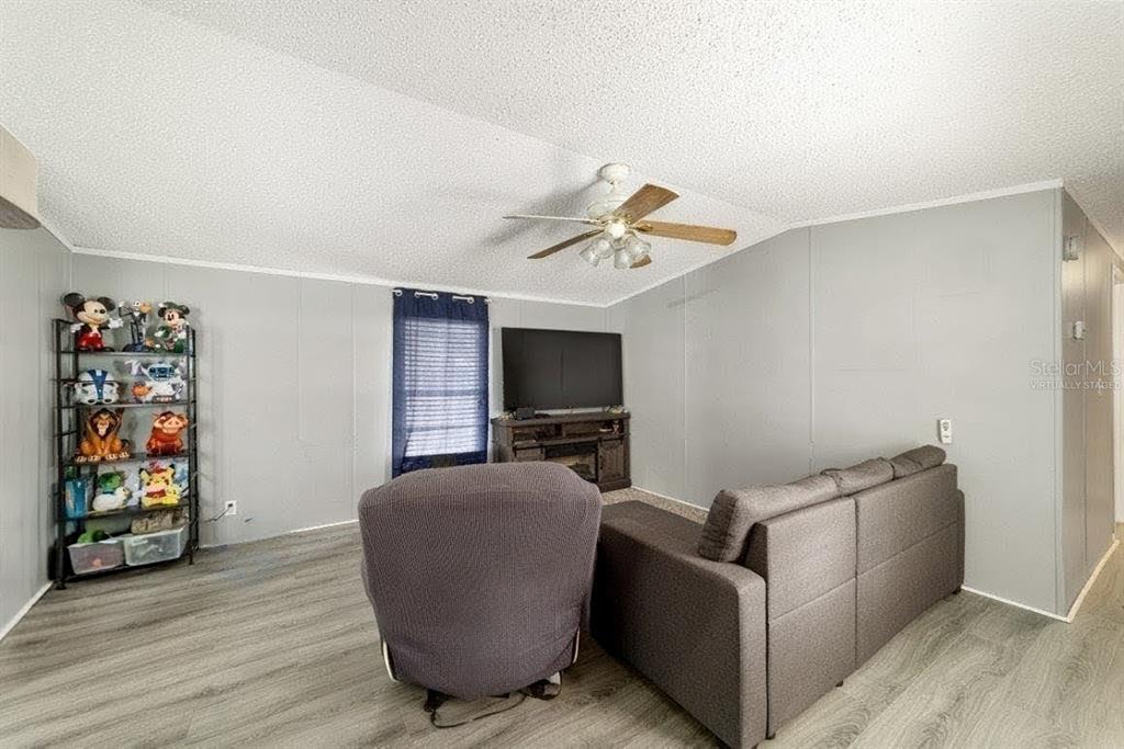 A living room features gray walls, wood-look flooring, a ceiling fan, and a television console — 13261 NE 155TH LANE, FORT MC COY, FL