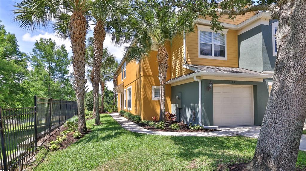 A two-story townhouse with a yellow and green exterior, a garage, and palm trees — 1102 BERKMAN CIRCLE, SANFORD, FL
