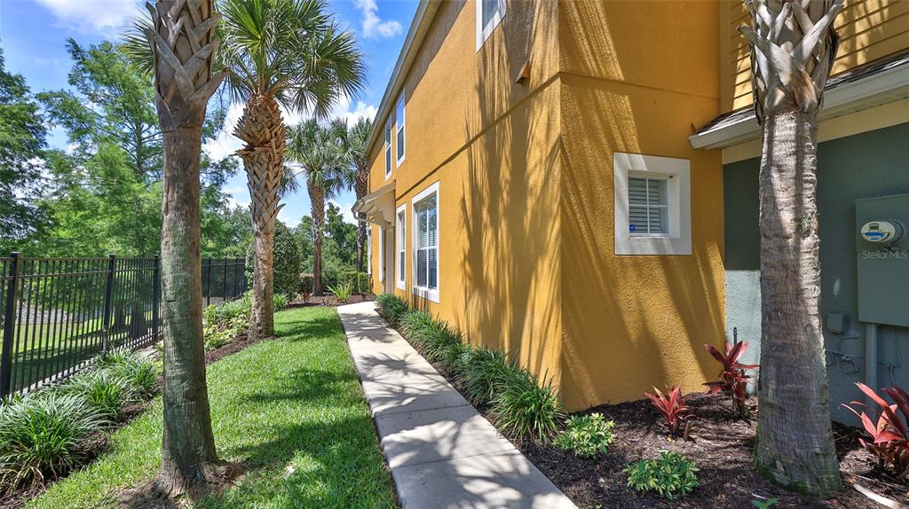 A concrete walkway runs along the side of a yellow stucco building with palm trees — 1102 BERKMAN CIRCLE, SANFORD, FL