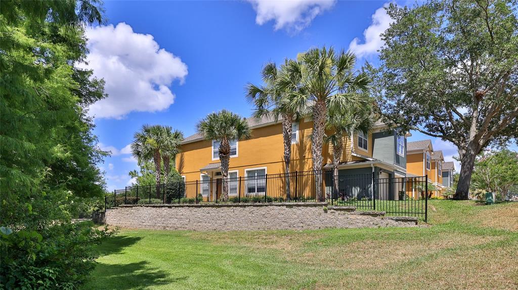 A yellow two-story house sits behind a black metal fence and a stone retaining wall — 1102 BERKMAN CIRCLE, SANFORD, FL