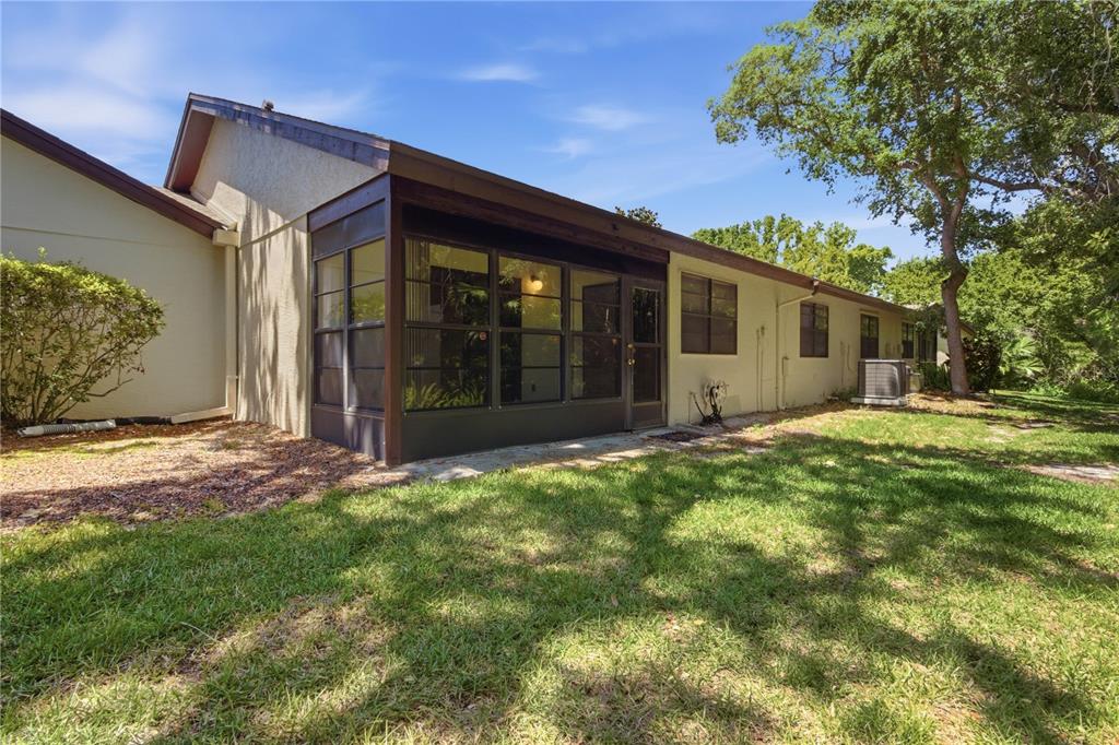 A view of the backyard showing a house with a screened-in porch and lawn — 2909 FIG COURT, PALM HARBOR, FL