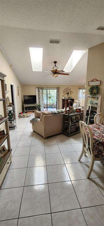 A living room with tile floors, a vaulted ceiling with skylights, and a ceiling fan — 2870 IDLEWEISE DRIVE, DELTONA, FL