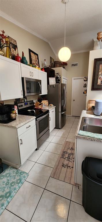 A kitchen features white cabinets, stainless steel appliances, a pendant light, and tiled flooring — 2870 IDLEWEISE DRIVE, DELTONA, FL