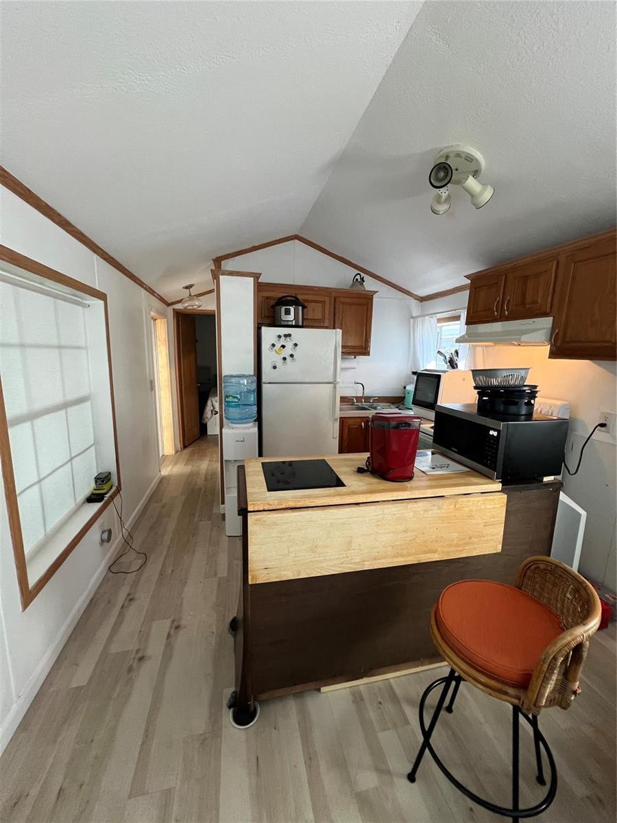 A small kitchen features wood cabinets, a portable island, and light-colored wood-look flooring — 6445 SE 51st Street, Okeechobee FL 34974, OKEECHOBEE, FL