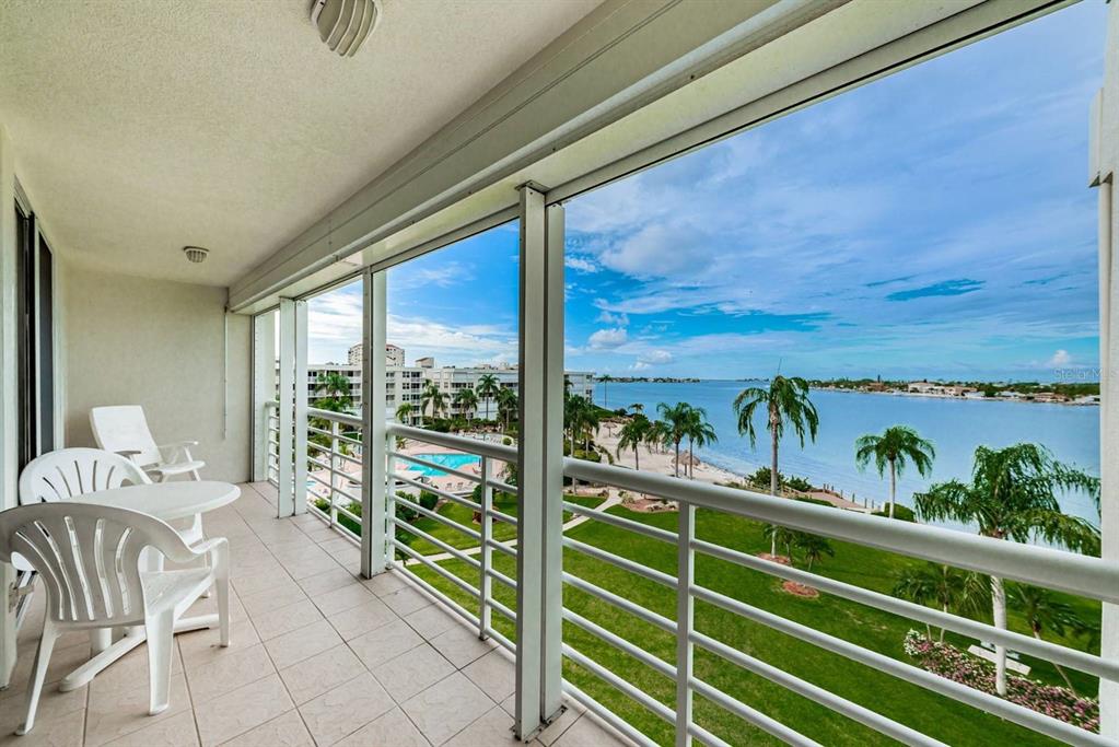 A balcony with white patio furniture overlooks a grassy lawn, a swimming pool, and water — 6001 BAHIA DEL MAR CIRCLE UNIT 527, ST PETERSBURG, FL