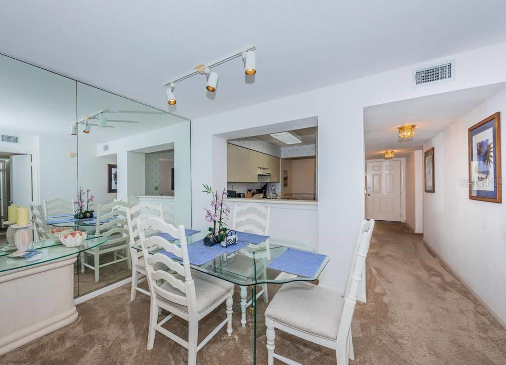 A dining area features a glass table, white chairs, a mirrored wall, and a kitchen pass-through — 6001 BAHIA DEL MAR CIRCLE UNIT 527, ST PETERSBURG, FL