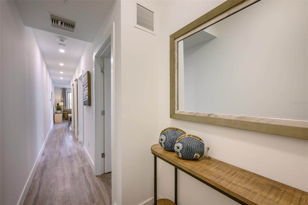 A hallway with light wood-look flooring leads past several doorways toward a living area — 1703 N TAMIAMI TRAIL UNIT 205, SARASOTA, FL