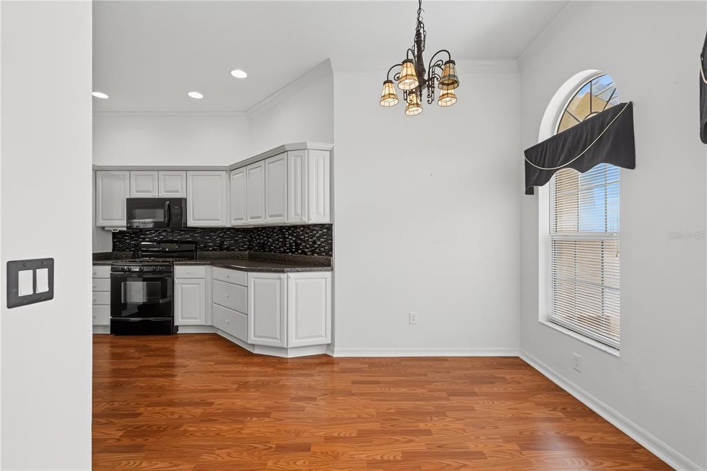 A kitchen with white cabinets, black appliances, dark countertops, and wood flooring — 556 KINGSTON WAY, THE VILLAGES, FL
